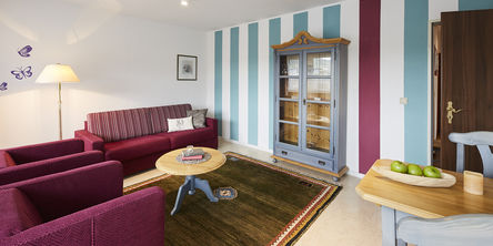 Loungebereich im Landhausstil mit hellblau und lila gestreifter Tapete und lilafarbenen Loungemöbeln 