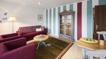 Loungebereich im Landhausstil mit hellblau und lila gestreifter Tapete und lilafarbenen Loungemöbeln 