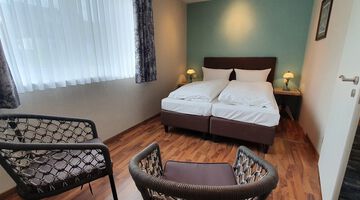 Schlafzimmer mit hellblauer Akzentwand, an der ein Doppelbett steht gegenüber von zwei Stühlen 