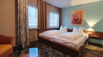 Gemütliches Doppelzimmer mit gemustertem Teppichboden und einer hellblauen Wand mit einem Rosengemälde