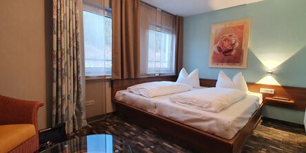 Gemütliches Doppelzimmer mit gemustertem Teppichboden und einer hellblauen Wand mit einem Rosengemälde