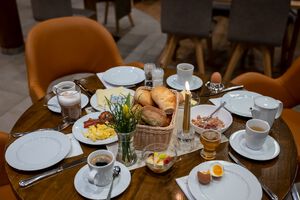 gedeckter Frühstückstisch mit vier Tellern, Kaffee, Brötchen, Eiern und einer Kerze