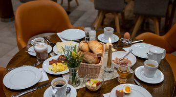 gedeckter Frühstückstisch mit vier Tellern, Kaffee, Brötchen, Eiern und einer Kerze