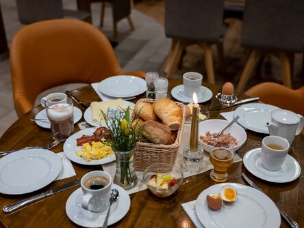 gedeckter Frühstückstisch mit vier Tellern, Kaffee, Brötchen, Eiern und einer Kerze