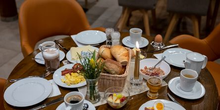 gedeckter Frühstückstisch mit vier Tellern, Kaffee, Brötchen, Eiern und einer Kerze