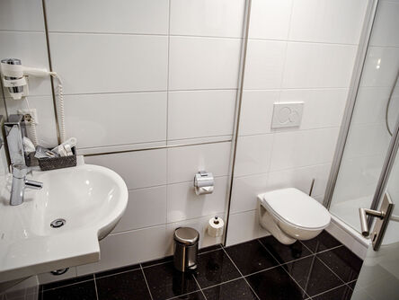 Blick in das geräumige Komfortzimmer mit gemütlichem Bett neben einer Couch gegenüber von zwei Sesseln und einem Holzschreibtisch 