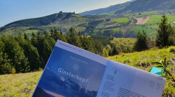 Person sitzt auf einem Berggipfel und liest einen Reiseführer