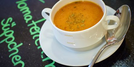 Eine Tomatencremesuppe vom Buffet, garniert mit frischen Kräutern, serviert in einer Suppentasse, die auf einem Unterteller steht.