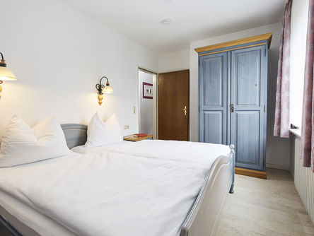 Ein großes Doppelbett steht  einem blauen Holzkleiderschrank gegenüber von einem Schrank 