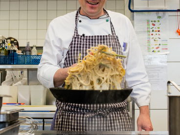 Koch schwenkt Essen in der Pfanne.