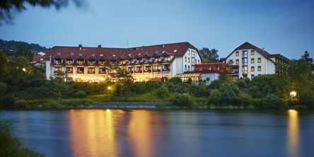 Beleuchtetes Hotel am Abend, idyllisch gelegen an einem ruhigen Fluss.